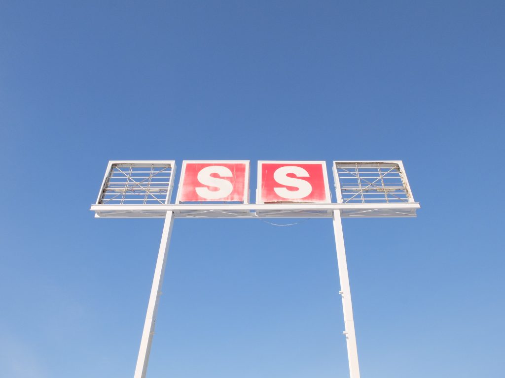 Old Esso sign with the e and o missing. The view is from the ground and the sign is backlit by a bright blue winter sky. 
