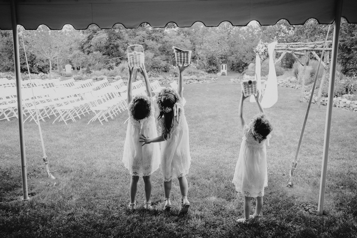 Black and white image of a group of flower girls in white dresses holding baskets to catch the rain.