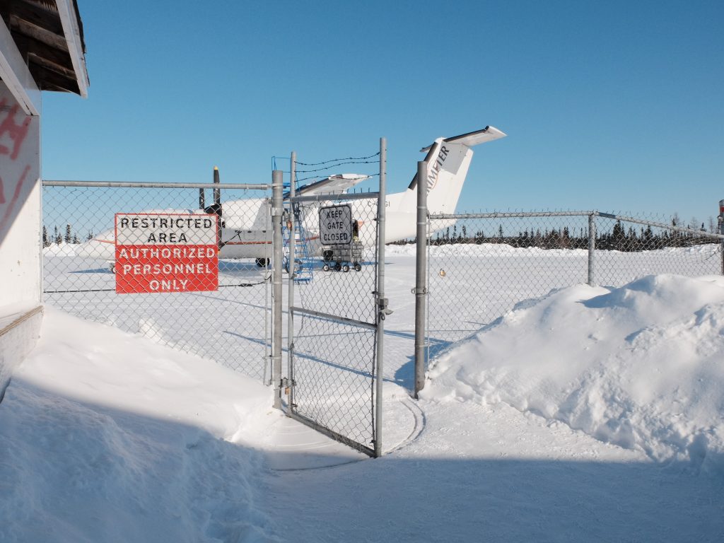 Image of an open gate fence with sign that says restricted area, authorized personnel only. Behind the fence sits a small plane.