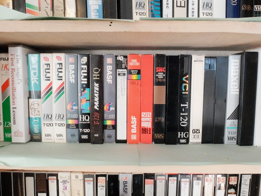 Photo of a bookshelf with old VHS cassette tapes.