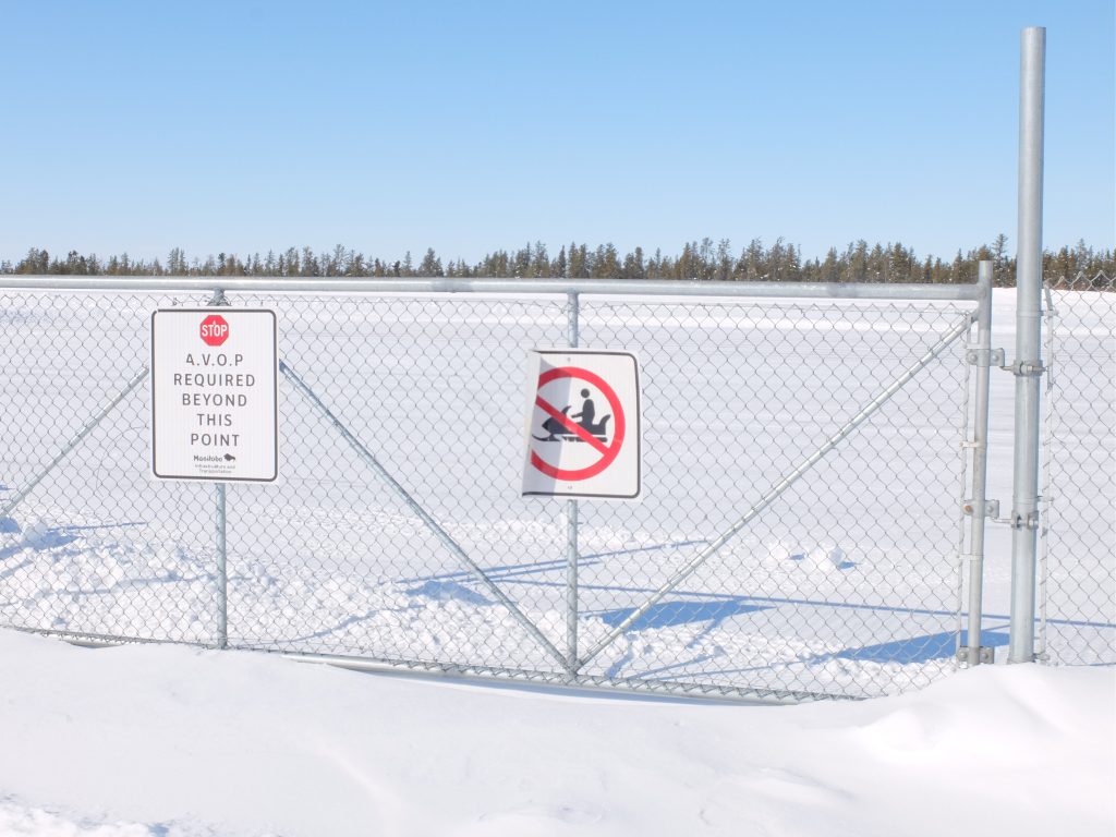 Image of a airfield metal fence with a sign that shows a no snow mobiles allowed. 