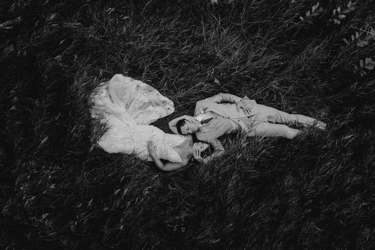 A bride and groom embracing each other while lying in long grass