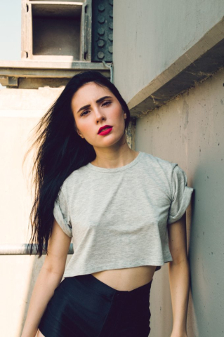 Model with black hair and red lipstick leans against a wall, photographed in the summer at Lockeport, Manitoba